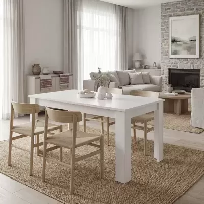 Sala de jantar com mesa branca e quatro cadeiras de madeira clara sobre tapete castanho claro, sofá bege e lareira em fundo de pedra.