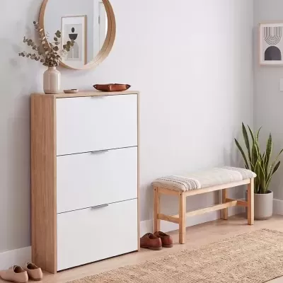 Móvel para sapatos branco e madeira com espelho redondo, banco estofado e planta num ambiente interior moderno