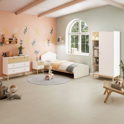 Quarto infantil com cama branca e móveis em madeira clara, parede rosa com pássaros, janela grande e tapete redondo cinza