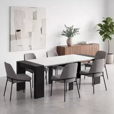 Conjunto de sala de jantar com mesa extensível branca e pés pretos, seis cadeiras cinzentas e aparador de madeira com planta
