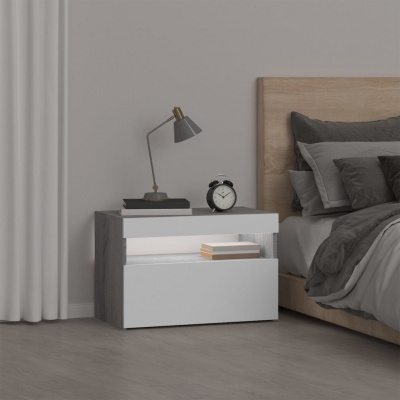 Mesa de cabeceira branca e cinzenta com candeeiro e relógio ao lado de cama com roupa de cama cinzenta