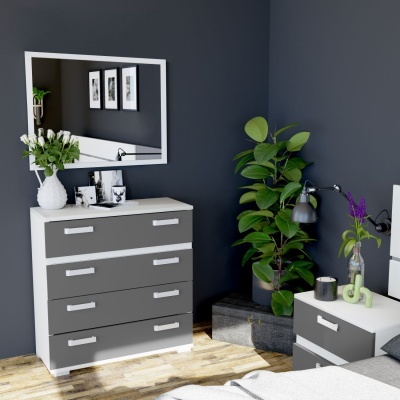 Cómoda cinzenta com moldura branca, decorada com flores, espelho em parede cinzento escuro, planta verde, mesa de cabeceira cinzenta e branca com lâmpada e flores roxas.