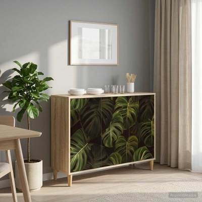 Aparador de madeira clara com padrão de folhas tropicais, utensílios e copos em cima, planta em vaso branco ao lado, parede cinzenta e cortinas bejes