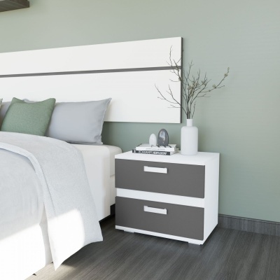 Mesa de cabeceira branca e cinzenta com gavetas, vaso branco e livros ao lado de cama com almofadas verdes e cinzentas