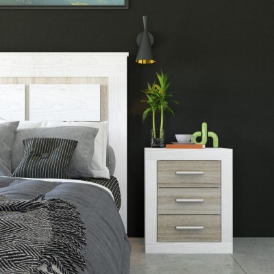 Mesa de cabeceira branca com três gavetas castanho-claro junto a cama cinza e candeeiro preto na parede preta