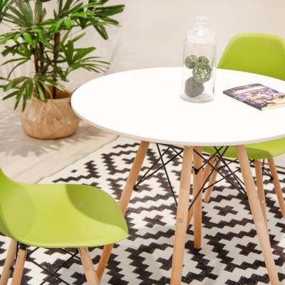 Mesa de jantar redonda branca com cadeiras verdes e tapete geométrico em sala iluminada