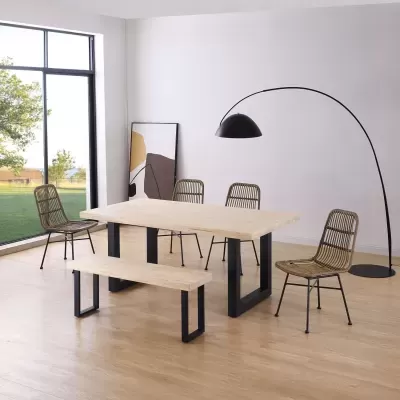 Mesa de madeira clara com pernas pretas, banco, cadeiras de rattan, candeeiro de pé preto e quadro abstrato num interior minimalista.