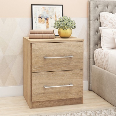 Mesa de cabeceira em madeira clara com decoração, junto a cama estofada cinza