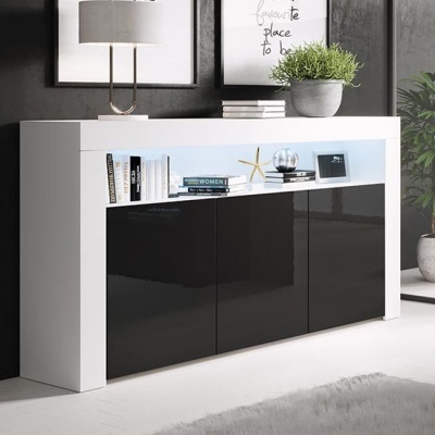 Aparador branco com portas pretas e prateleira iluminada, decorado com livros, lâmpada, planta e quadros cinzentos na parede