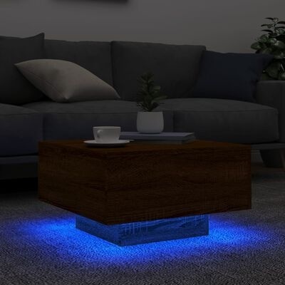 Mesa de centro quadrada em madeira com base de vidro iluminada a azul em sala com sofá cinzento