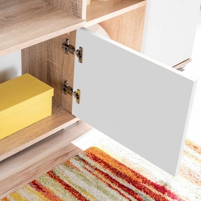 Móvel de madeira clara com porta branca aberta e caixa amarela no interior junto a tapete colorido.