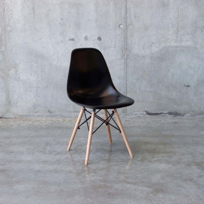 Cadeira preta com pernas de madeira clara contra parede de cimento