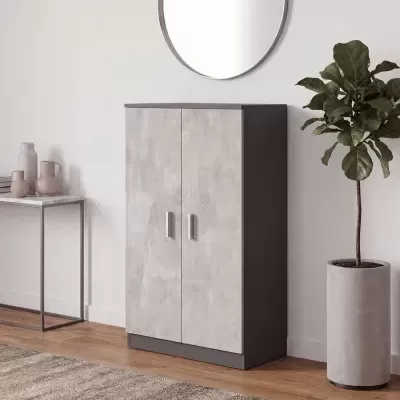 Armário de madeira cinzento de duas portas junto à parede com espelho redondo, mesa com jarros e vaso alto com planta verde