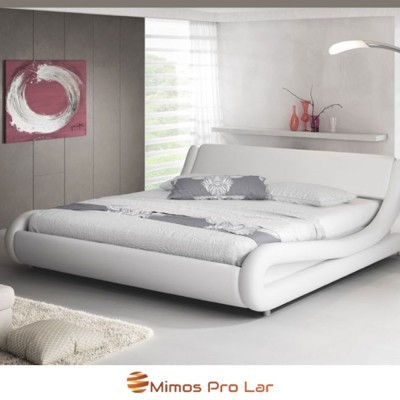 Cama estofada branca com roupa de cama cinza e almofada floral, quadro abstrato na parede e lâmpada curva