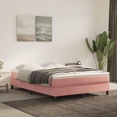 Cama de casal rosa estofada com roupa de cama cinza e branca, parede branca com quadros e planta verde ao lado