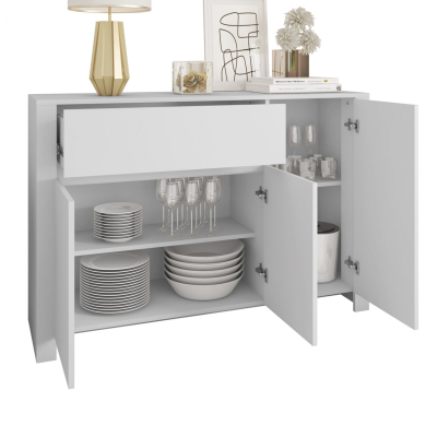 Aparador branco com portas abertas mostrando louças e decoração em cima.
