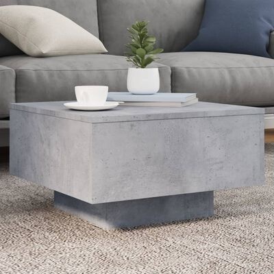 Mesa de centro cinzenta estilo betão com planta, livreto e chávena numa sala com sofá e tapete bege