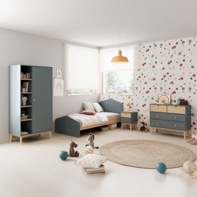 Quarto infantil moderno com cama azul, armário e cómoda cinza, papel de parede colorido, tapete redondo natural e brinquedos no chão.