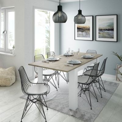 Mesa de jantar de madeira clara com seis cadeiras metálicas pretas e assentos brancos, luminárias pendentes pretas e quadros na parede em ambiente moderno