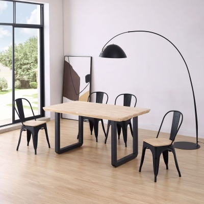 Mesa de jantar retangular de madeira clara com cadeiras metálicas pretas, em sala com chão de madeira e candeeiro de pé