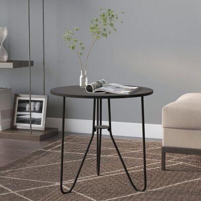 Mesa de apoio redonda preta com patas finas de metal, revista e vasos com plantas numa sala cinzenta