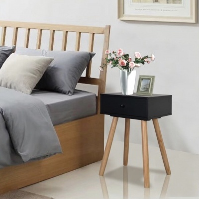 Cama de madeira com roupa de cama cinzenta e mesa de cabeceira preta com flores rosas