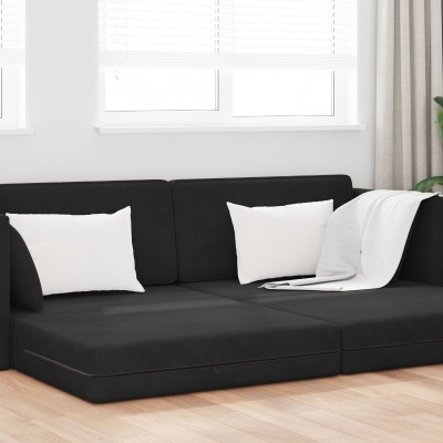 sofá modular preto com almofadas e manta branca numa sala com janelas