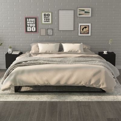 Cama moderna com edredão bege, manta cinza e mesas de cabeceira pretas num quarto com parede de tijolos cinzenta e quadros decorativos.