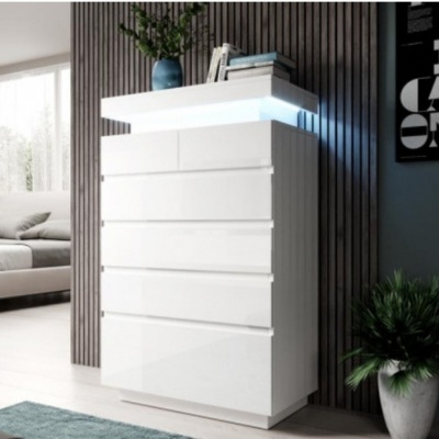 Móvel branco lacado com seis gavetas junto a parede de madeira escura e planta em vaso branco