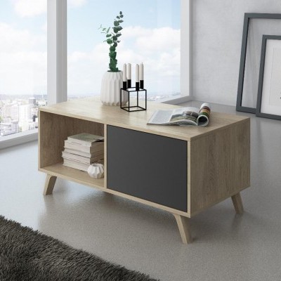 Mesa de centro de madeira clara com porta cinza escuro, jarra branca com planta, castiçal preto e molduras ao fundo.