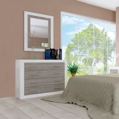 Cómoda com gavetas, espelho, jarro com ramo seco, livros, planta e cama com manta bege junto a janela grande