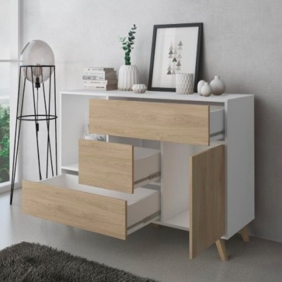 Cómoda branca com gavetas e porta de madeira clara, decorada com vasos, livros e quadro, ao lado candeeiro de pé