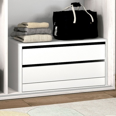 Móvel branco com gavetas e roupa dobrada com mala acima