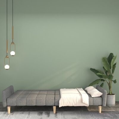 Sofá-cama cinzento em tecido com pernas de madeira, lençol branco, almofadas, lâmpadas douradas pendentes e planta em vaso cinzento