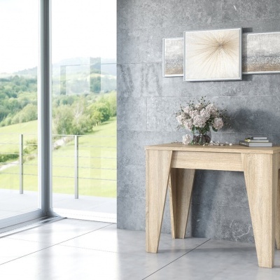 Mesa pequena de madeira clara contra parede cinzenta com vasos e quadros, ao lado de porta de vidro