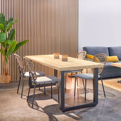 Mesa de jantar retangular de madeira com cadeiras metálicas e almofadadas em sala com sofá e planta