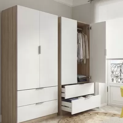 Dois roupeiros modernos em madeira clara e portas brancas, com gavetas abertas e roupas visíveis, num quarto claro com janela e tapete redondo
