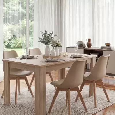 Mesa de jantar em madeira clara com cadeiras bege e decoração com flores em sala iluminada