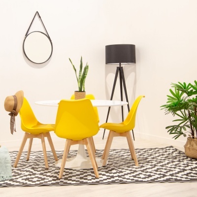 Mesa branca com quatro cadeiras amarelas e tapete geométrico preto e branco num interior com candeeiro, espelho e plantas