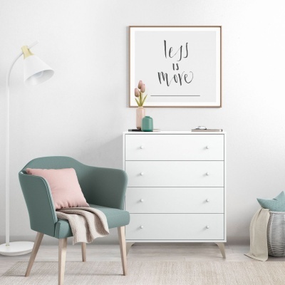 Cadeira verde estofada, cómoda branca, lâmpada de pé, quadro com texto 'less is more', vaso com flores e cesto com almofadas