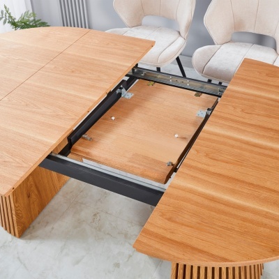 Mesa extensível de madeira aberta com estrutura metálica e cadeiras estofadas ao fundo