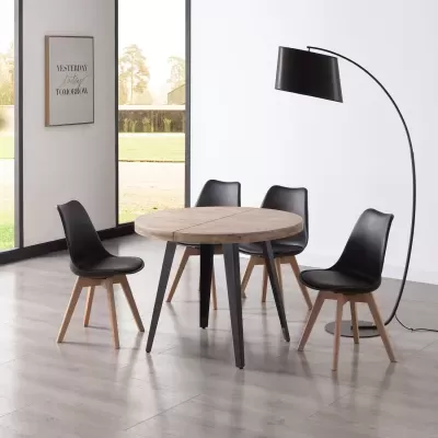 Mesa de jantar redonda em madeira clara com cadeiras pretas e lâmpada arco preta num espaço moderno.
