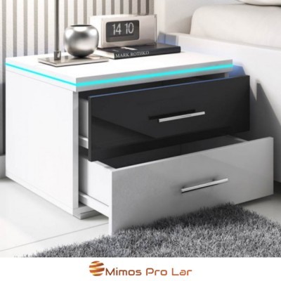 Mesa de cabeceira branca com gavetas preta e branca, relógio digital 14 10, livro e objeto decorativo prateado ao lado de sofá branco