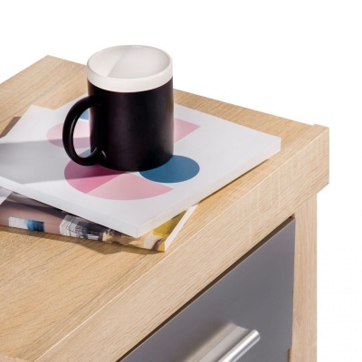 Caneca preta e branca sobre livro com círculos coloridos apoiado em mesa de madeira clara com gaveta cinza