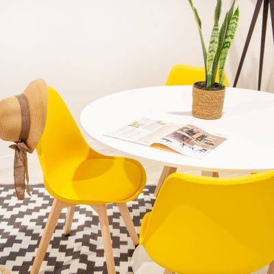 Mesa redonda branca com cadeiras amarelas e vaso com planta