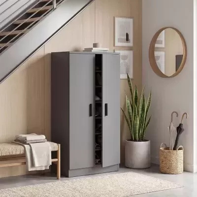 Armário cinzento sob escada com banco, planta, tapete, guarda-chuvas e decoração na parede
