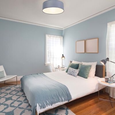 Quarto com cama de casal decorada, paredes azul claro e móveis simples