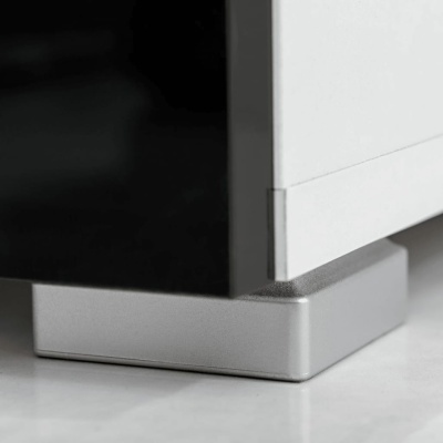 Canto inferior de móvel branco com base metálica prateada sobre chão claro