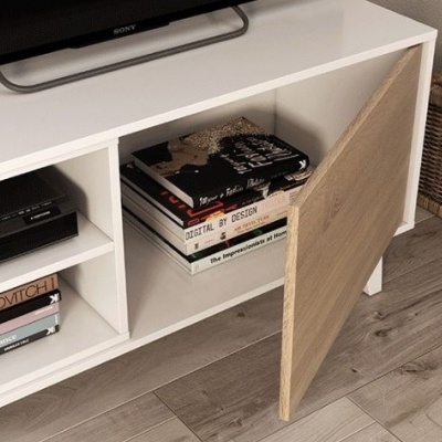 Móvel branco com porta de madeira clara, livros e cesta de vime ao lado num chão de madeira cinza