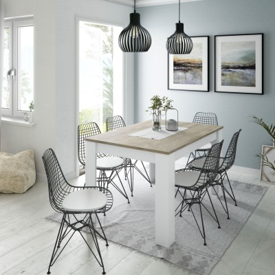 Mesa de jantar com tampo de madeira clara e cadeiras pretas aramadas com assentos brancos num ambiente com parede azul clara e quadros